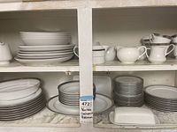 Multiple stacked plates, bowls and a butter dish on lower shelf