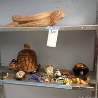 Full shelf view showing carved wooden turtle on top shelf and ceramic turtle cookie jar with small figurines and brass bell on bottom shelf.