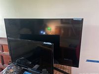 Two Samsung TVs shown together, 23 inch TV in front of 40 inch TV, both powered off and reflecting room light.