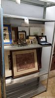 Wide shelf display with all artwork and metal decorative sculptures visible, showing variety of styles and framing