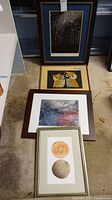 Four framed artworks arranged vertically on floor showing various styles including night forest scene, stylized owls, abstract colors, and circular designs.