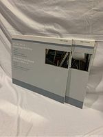 Photo of two packaged beveled edge wall mirrors stacked against a fabric backdrop. Boxes show product name and size.