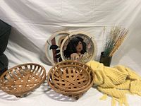 Three round wooden wall decorative baskets, three round art pieces with female portrait and floral designs, tall vase with dried grass, yellow knitted blanket.