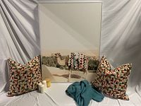 Photo of large framed camel art with two multicolor decorative pillows, teal blanket, and four candles