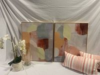 Photo showing the two abstract art pieces alongside the artificial orchid, glass lamp, and pink-white striped cushions.