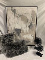 Large abstract art with neutral colors, paired with two fluffy grey cushions and two black spike sculptures
