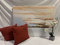 Full view of the contemporary wall art painting with two rust-colored cushions in front and faux white orchid on the side.