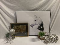 Front view of office decor including framed horse art, black desk lamp, metal sculptures, artificial plants, and small globe