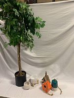 Full view of the artificial tree with green leaves and four small decorative items on the ground