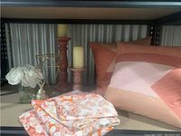 King-size bedding items including folded floral duvet cover and pillowcases, decorative cushions, wooden candlesticks with candles, glass vase with artificial flowers, and gold candle holder.