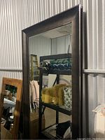Large full-length standing mirror with wide dark brown wooden frame and visible chips on the edges.
