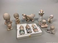 Full view of nine assorted ceramic figurines arranged on table; includes children, horse, and smaller seated figures with pastel coloring.