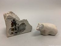 Two Inuit soapstone carvings: a detailed paperweight signed SIKU depicting an Inuit individual with a sled, and a separate smooth bear figurine.