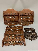 Four wooden wall-mounted displays holding over 60 vintage collector's souvenir spoons. Spoons feature enamel and metal handles with regional and commemorative icons.