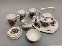 Photo showing the full tea set including teapot, creamer, sugar bowl, cake plate, condiment plates, and mugs arranged on table