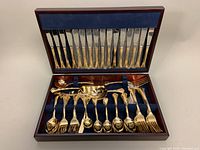 Open chest showing upper compartment with 16 gold-plated dinner knives and lower compartment with assorted utensils