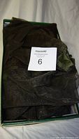 Folded dark green bug netting inside a box with a label showing the lot number.