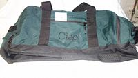 Front and side view of the green and black Ciao branded sport equipment bag showing the outer zipped pocket and black straps.