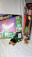 Photo of the Thunder Cats sticker plak-it board, Star Wars Qui-Gon Jinn lightsaber in box, John Deere front loader toy, and two wooden cars.