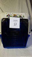 Front view of blue and white plastic pet crate with front metal wire door and seller auction number paper attached