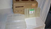 Beige Flambeau 1999 Adventurer tackle box with two clear parts boxes placed in front on white cloth-covered surface