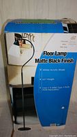Box for a floor lamp with matte black finish, white acrylic shade, 63" height, and 6.3' height stated on box. Shows a picture of the lamp design.