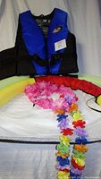 Blue and black Nautilus adult life jacket with multicolored flower lei and floating seat visible behind with pool noodle attached.