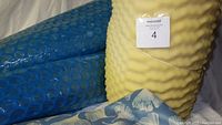 Two blue bubble sleeping mats, yellow egg crate foam pad and blue air pillow with floral fabric cover shown folded against wall.