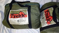 Two green Trekk sleeping bags packed in nylon storage bags with labels showing brand and model