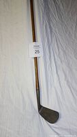 Full length photo of a vintage left handed golf club with a hickory shaft lying against a fabric background, showing the entire club including the head and shaft.