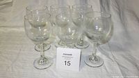 Six clear glass wine glasses displayed on a flat surface with white background, small etched pattern near base of bowl visible on each glass.