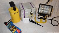 Photo showing the 250W workshop light with yellow 4-in-1 mounting stand and its packaging along with the Ever Ready 2-way portable lantern in new package including hanging stake and bulb.