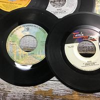Close-up of several 45 RPM vinyl record labels including Warner Bros and Tamla Motown with visible titles and artists.
