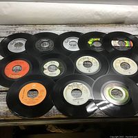 12 black 45 RPM vinyl records laid out showing center label details and colors, identifying some artists and labels.