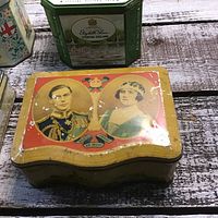 Curved rectangular tin with royal portraits showing wear and age.