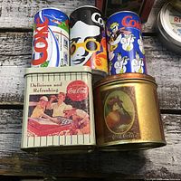 Front view of Coca-Cola cans and two collectible Coca-Cola tins showing artwork and condition