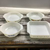 Four Fire King milk glass bowls arranged on wooden surface, each displaying distinct vintage patterns.