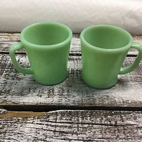 Two Fire King jadeite coffee mugs side by side, showing front and handles.