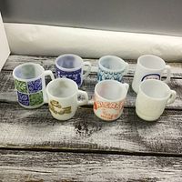 Seven Fire King coffee mugs with different designs displayed on a wooden surface.