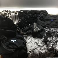 Various women's casual clothing items piled together, showing different fabric textures and colors including black, gray and patterns