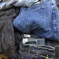 Several pairs of ladies jeans in varying shades of blue and black denim, folded and stacked showing back pockets and waistbands, including one labeled 'Jones'.