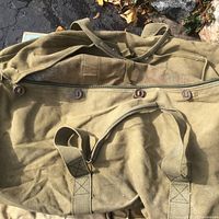 Large olive drab canvas duffel bag showing button closures and carrying handles.