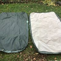 Two deflated Ozark Trail mattresses, one green and one beige, laid on grass outdoors.