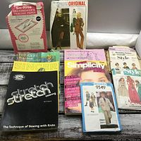 Photo showing several sewing books and patterns including So-Rite dressmaker's tracing paper, Paris Original pattern for a suit, and multiple sewing instructional books.