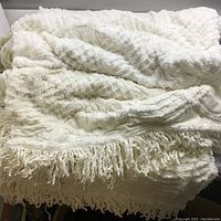 White vintage bedspread with textured diamond pattern spread out showing fringe tassels on edges.