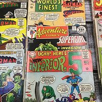Close-up of comic book covers showing titles Superman, World's Finest, Batman, Adventure Comics featuring Supergirl, and The Inferior 5 with colorful illustrations and vintage cover prices.