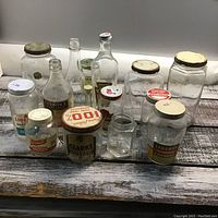 Full view of all 14 vintage glass jars on wooden surface showing variety in shapes, sizes, and lids.