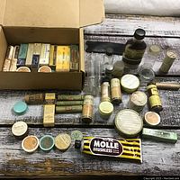 Top-down view of vintage medical and grooming items arranged on wooden surface, including open box with small boxes inside, tubes, jars, and bottles.