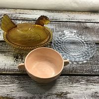 Top view of three vintage glass items including a bubble glass plate, carnival glass chicken bowl, and pink bowl.