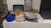 Wide view of bakeware lot showing multiple pizza pans, cooling racks, glass and metal dishes, bakeware items arranged on a table.